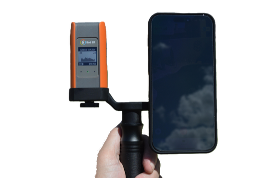 Hand holding a device with an orange and gray panel next to a smartphone on a white background